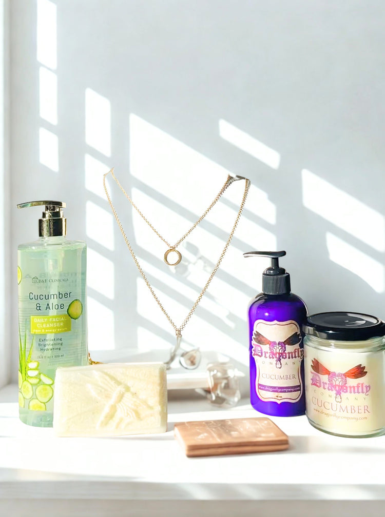 Bathroom products including a lotion, soap, and candle, facial cleanser and a necklace on a windowsill with sunlight streaming in.