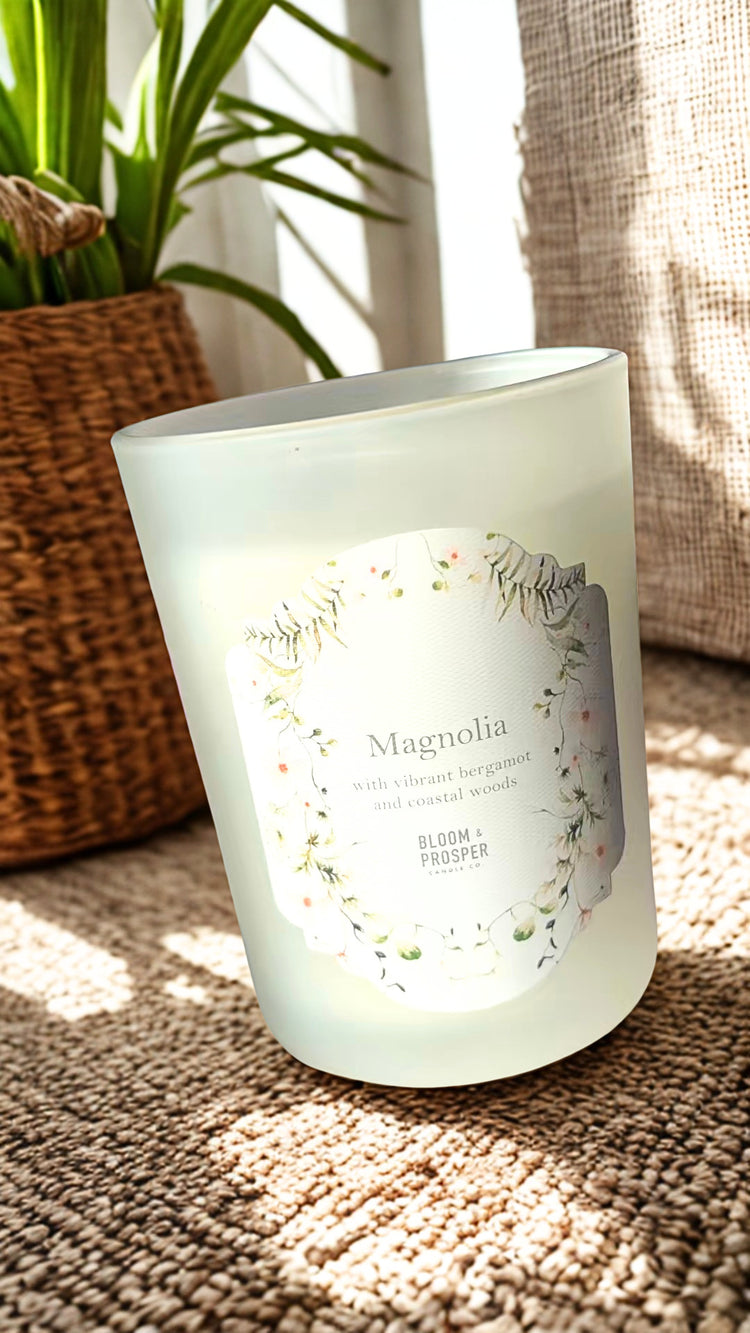 Frosted candle with 'Magnolia' branding on a textured surface