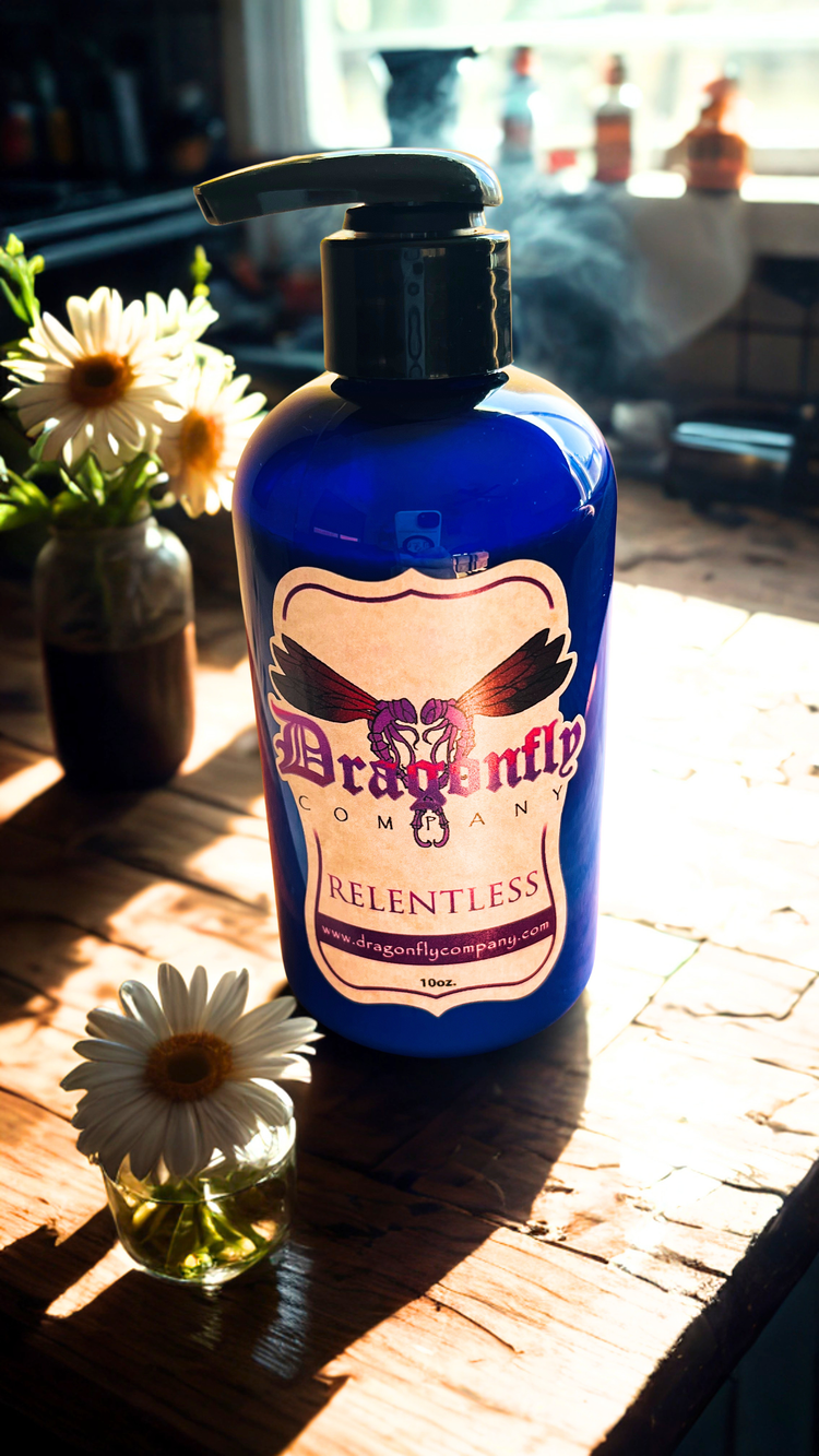 Bottle of Dragonfly Body Lotion Relentless on a wooden surface with flowers.
