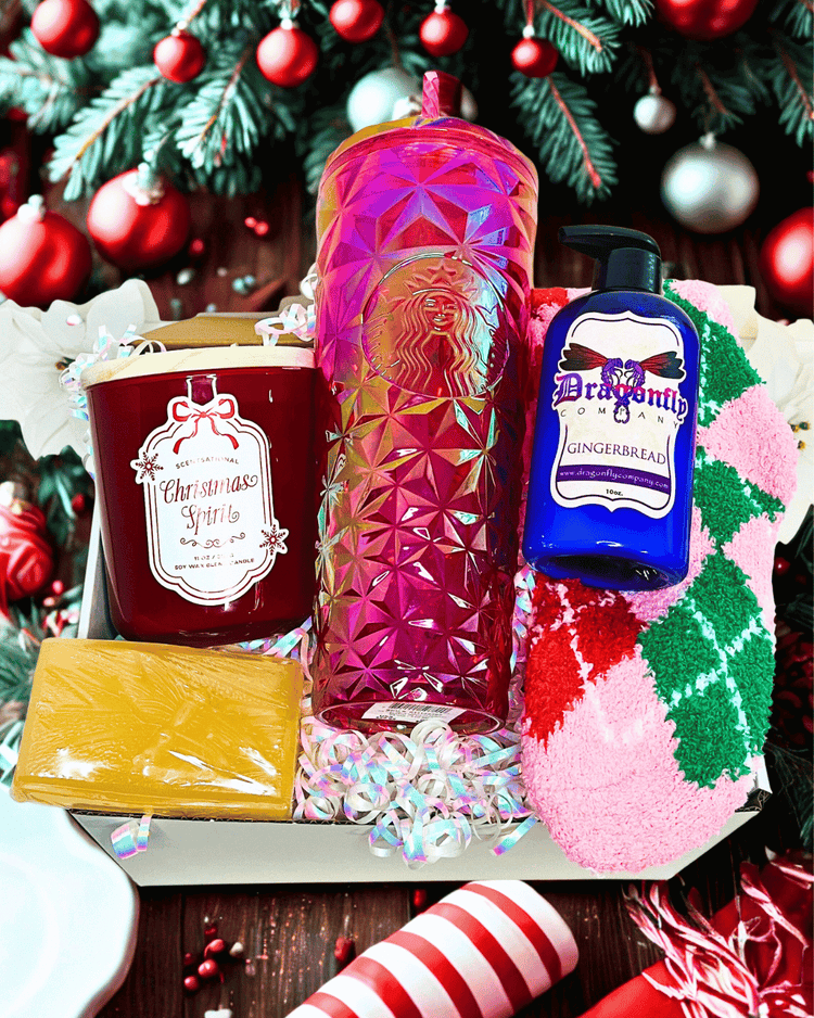 Holiday gift set with a candle, tumbler, and other items in front of a Christmas tree.