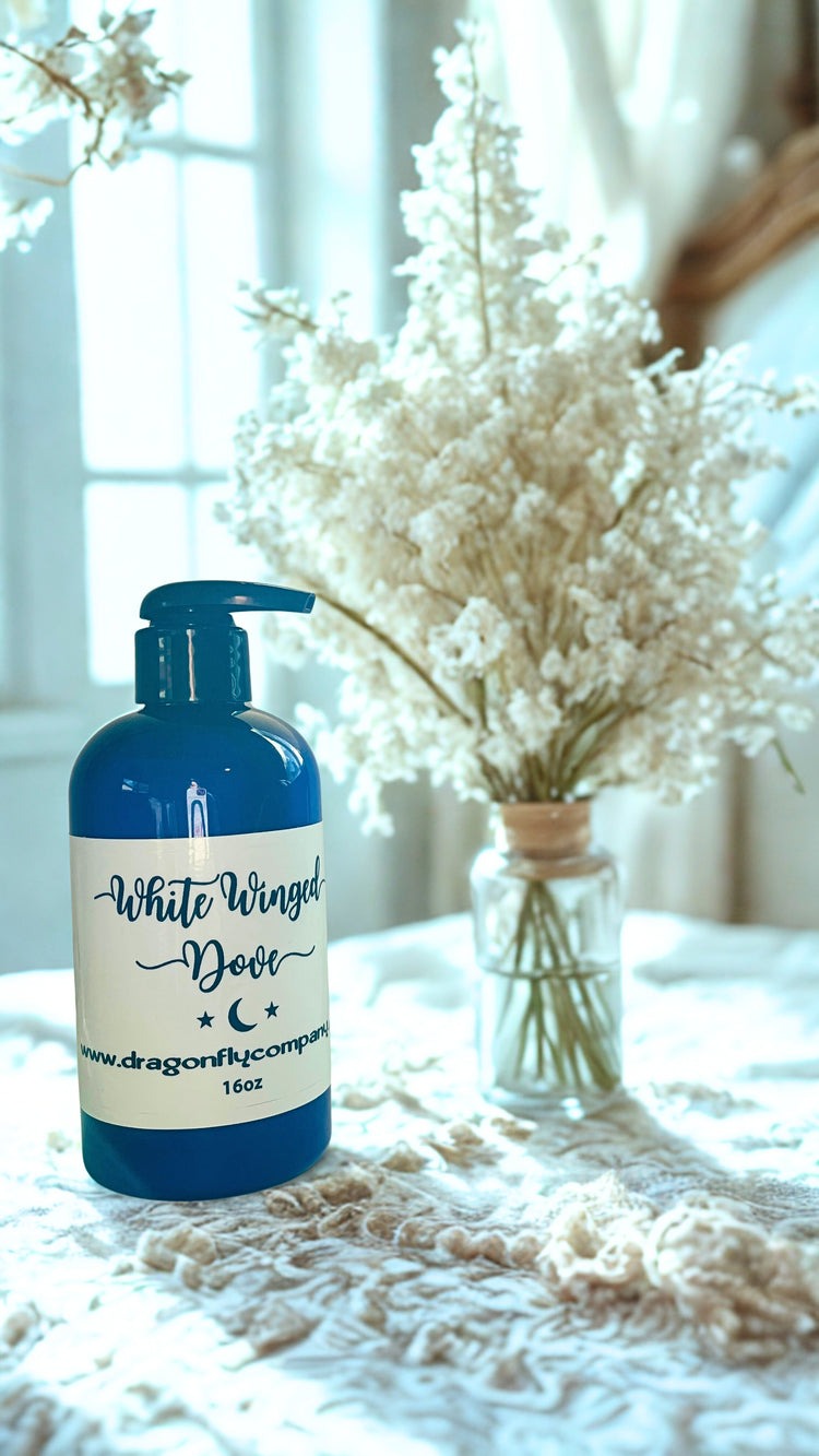 Bottle of 'White Winged Dove'lotion on a textured surface with decorative flowers in the background