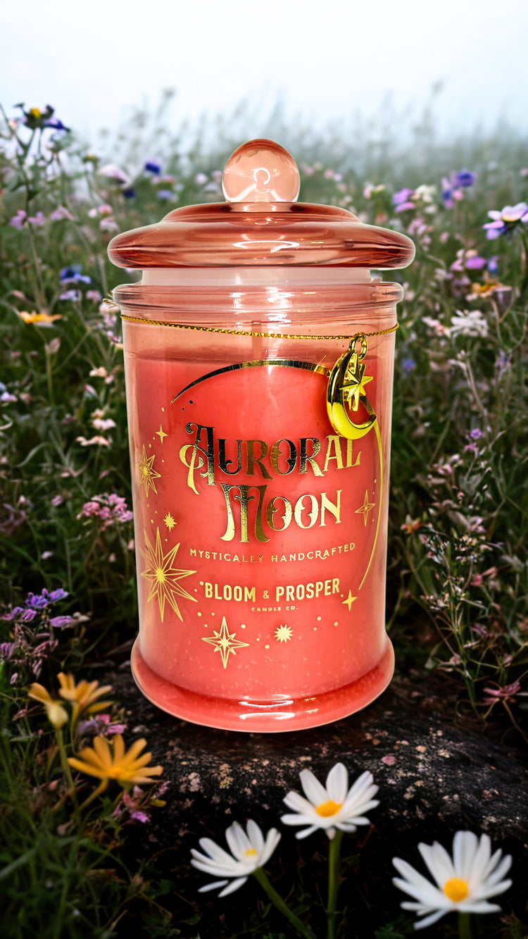 Pink candle jar labeled 'Auroral Moon' in a field of flowers