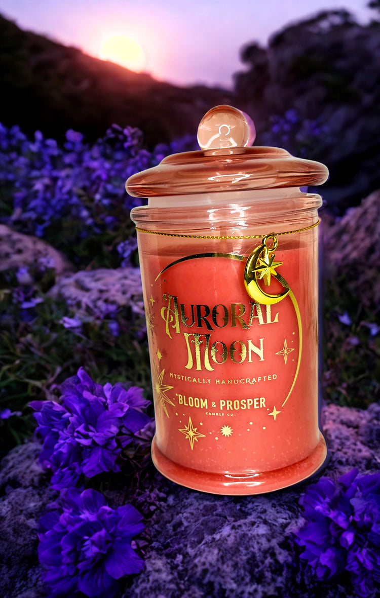 Candle jar labeled 'Auroral Moon' surrounded by purple flowers with a sunset background