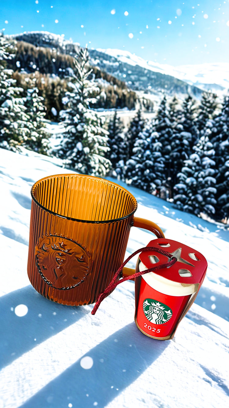 Amber Starbucks mug and red Starbucks ornament in the snow with a mountainous background