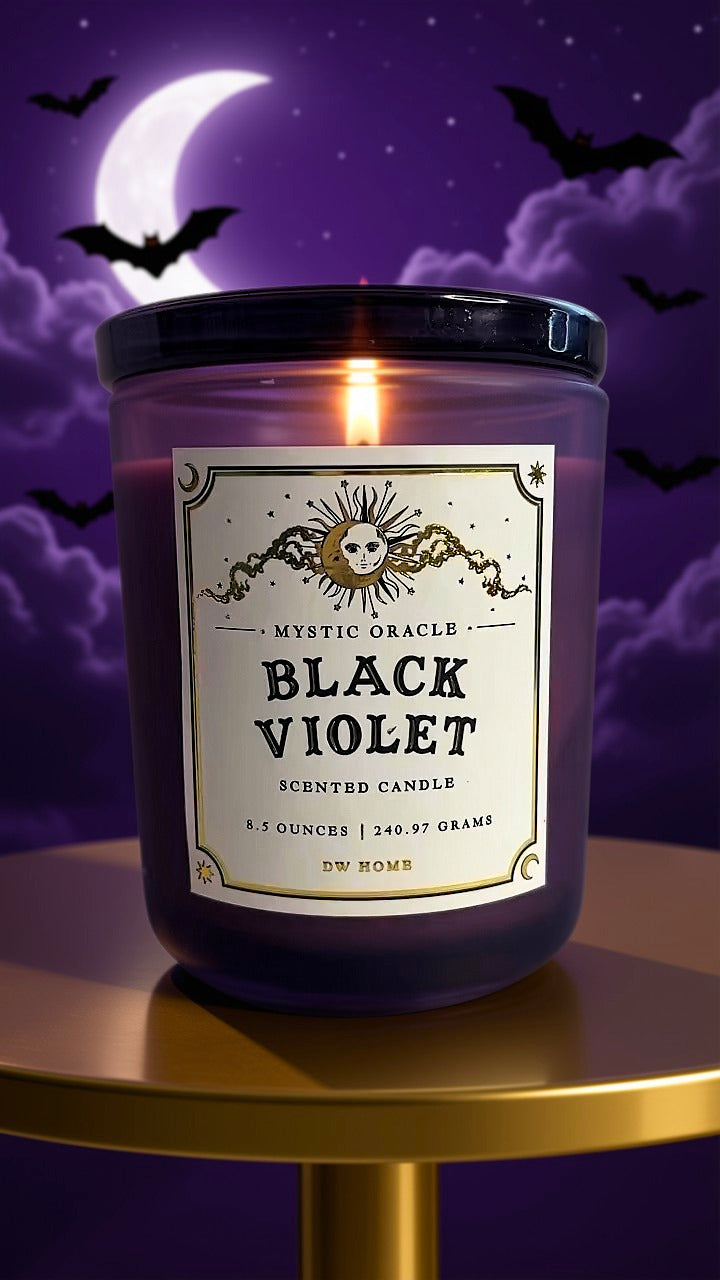 A lit scented candle in a purple glass jar sits on a gold table against a Halloween night background with a crescent moon, clouds, bats, and a purple sky. The label reads 'Mystic Oracle Black Violet Scented Candle' 