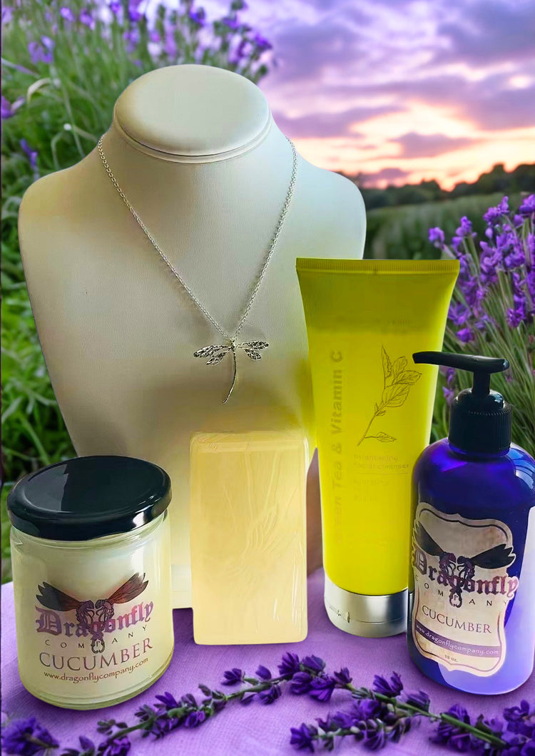 A curated collection of Dragonfly Cucumber skincare and wellness products arranged on a purple surface with lavender sprigs and a blurred lavender field sunset background.