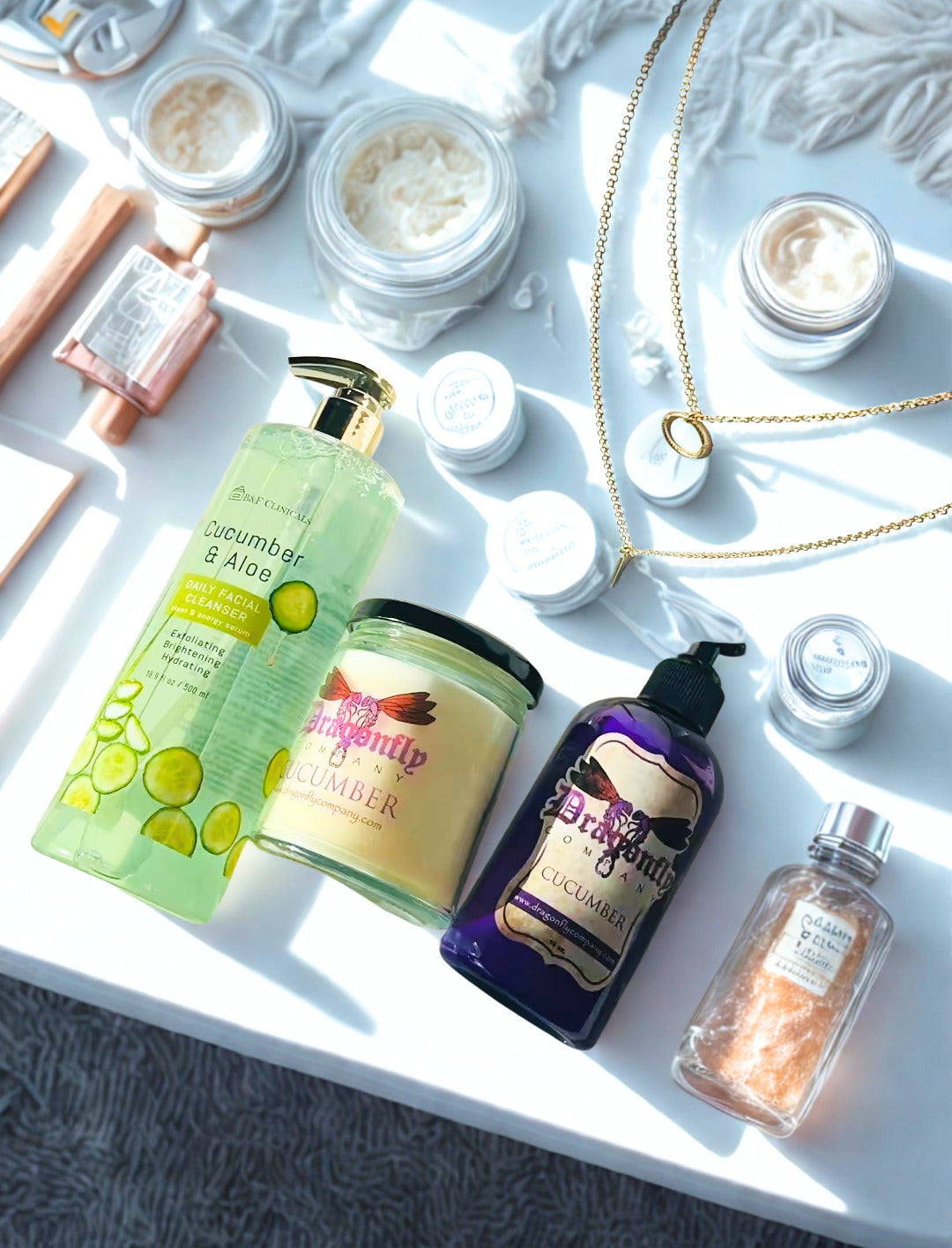 Collection of body care products including cucumber facial cleanser, candle , lotion, soap and necklace  on a textured surface.