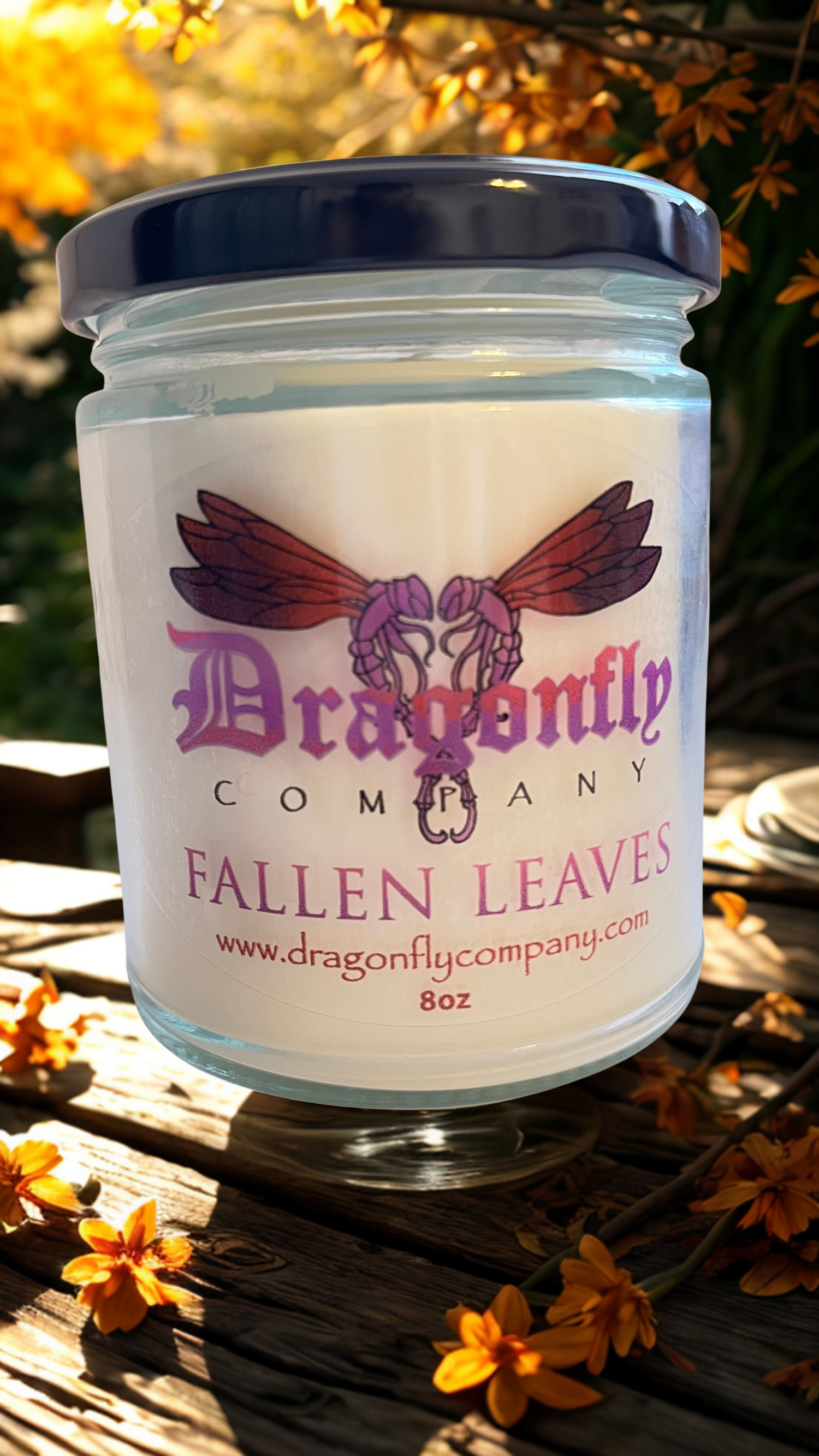 Jar of 'Fallen Leaves' candle from Dragonfly Company on a wooden surface with flowers.
