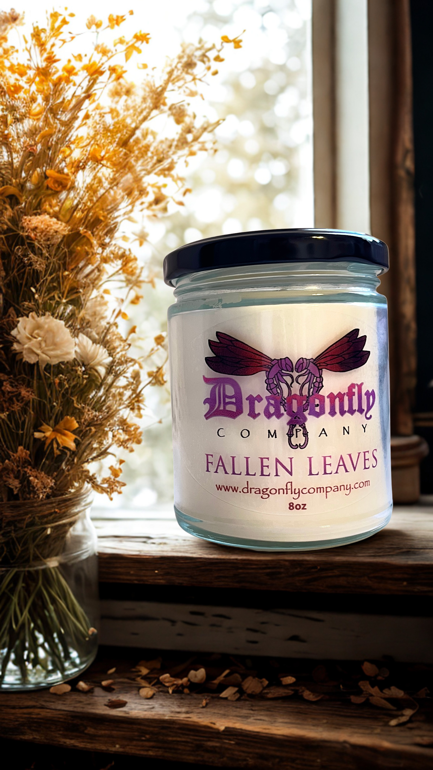 Jar of 'Fallen Leaves' candle from Dragonfly Company on a windowsill with dried flowers.