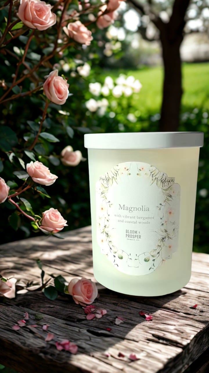 Candle labeled 'Magnolia' on a wooden surface with pink flowers in the background