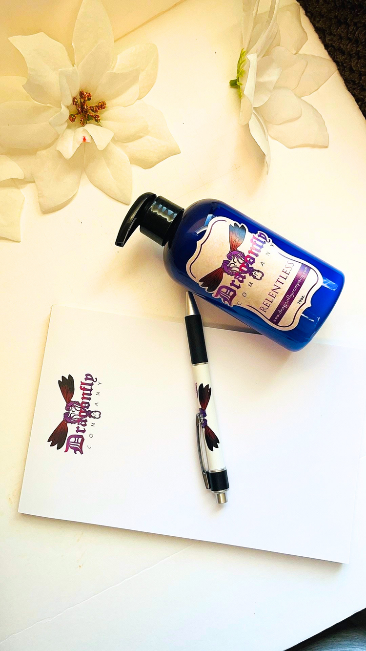 Bottle of Relentless Body Lotion with a pen on a white surface with flowers in the background