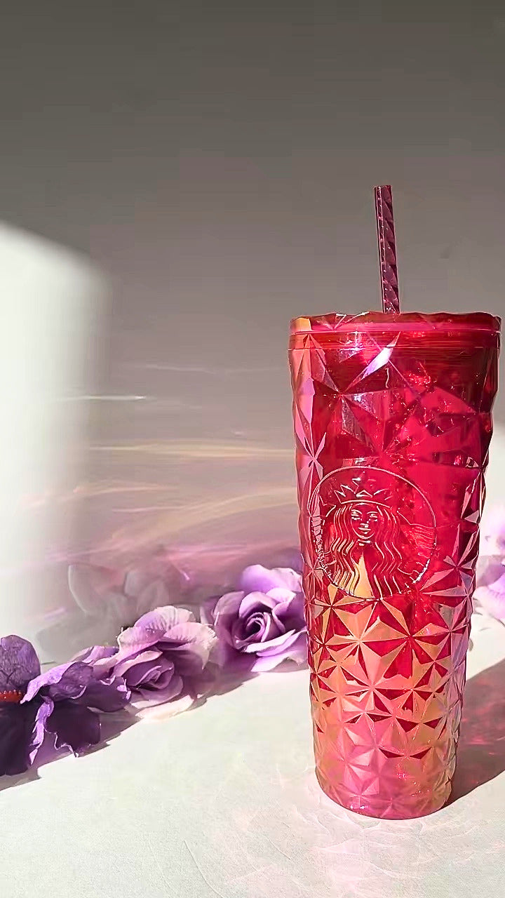 A red faceted textured  tumbler cup with a matching red striped straw, featuring an embossed Starbucks siren logo, set against a light gray background with decorative purple flowers on the left.