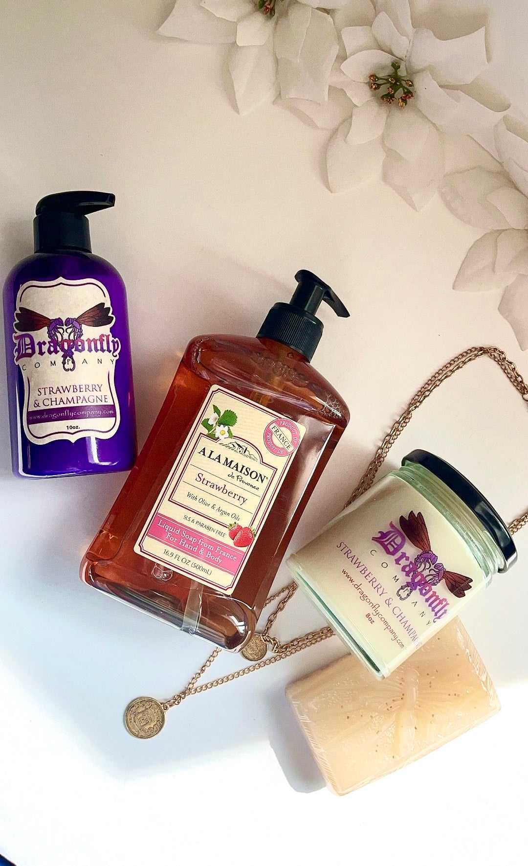 Strawberry  and Champagne beauty products including a bottle, jar, and soap on a light background with flowers.