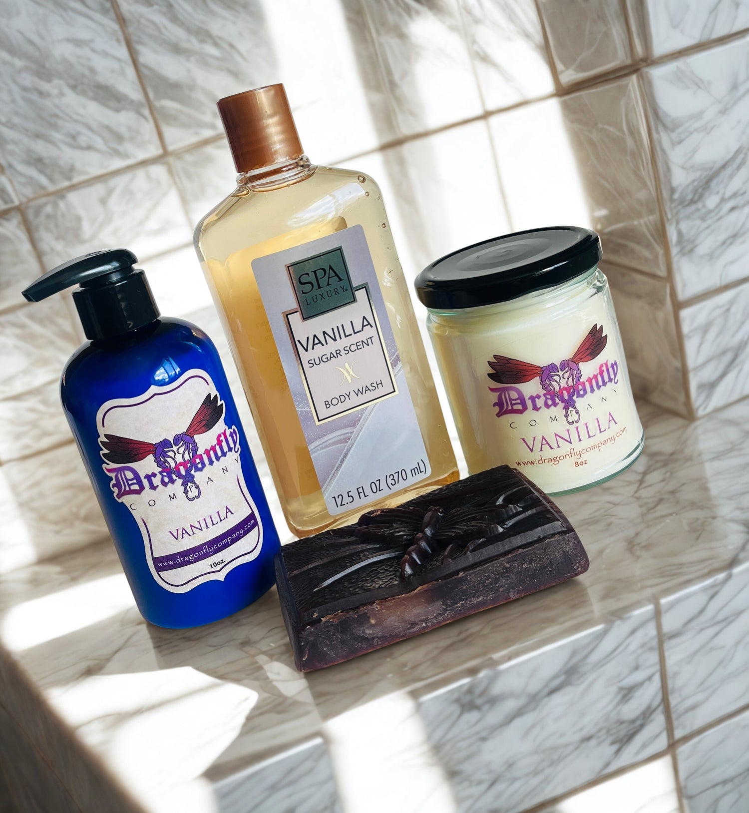 Vanilla soap lotion candle body wash and shower puff  on a tiled surface.