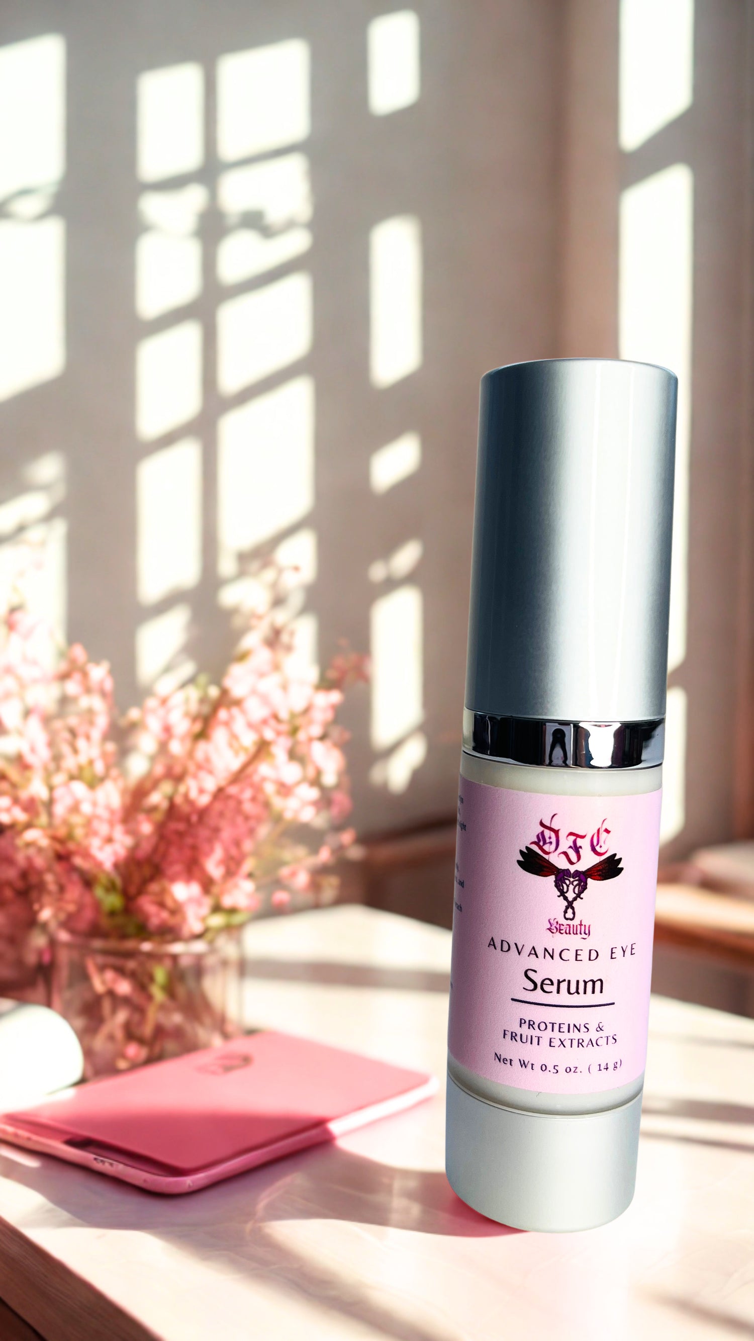 A bottle of DFC Skincare Advanced Eye Serum stands on a tabletop in a sunlit room with window shadows, next to a pink notebook and flowers.
