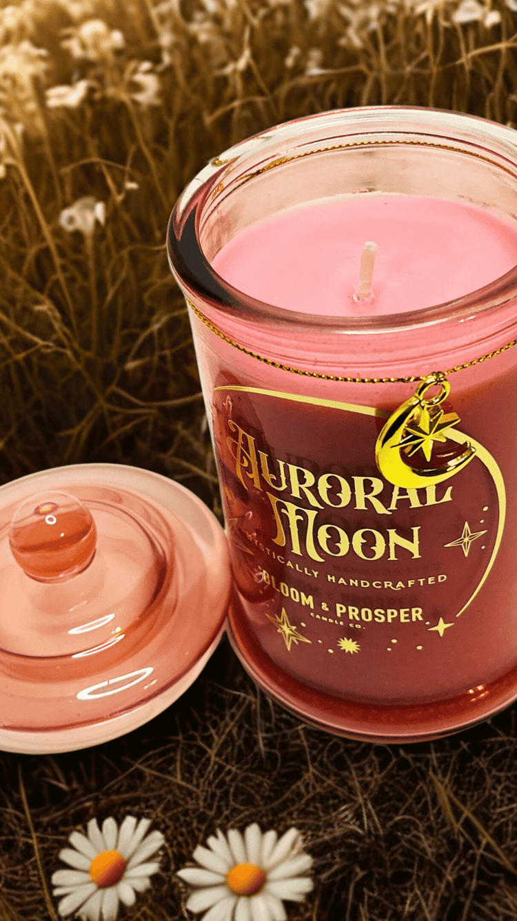 Pink candle with 'Auroral Moon' branding in a natural setting with flowers.