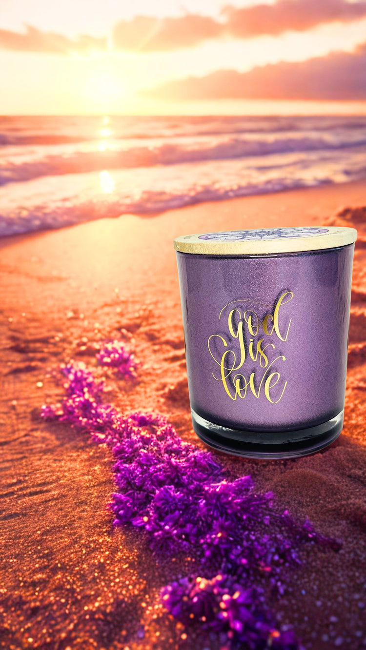 Purple candle with 'God is Love' text on a beach at sunset
