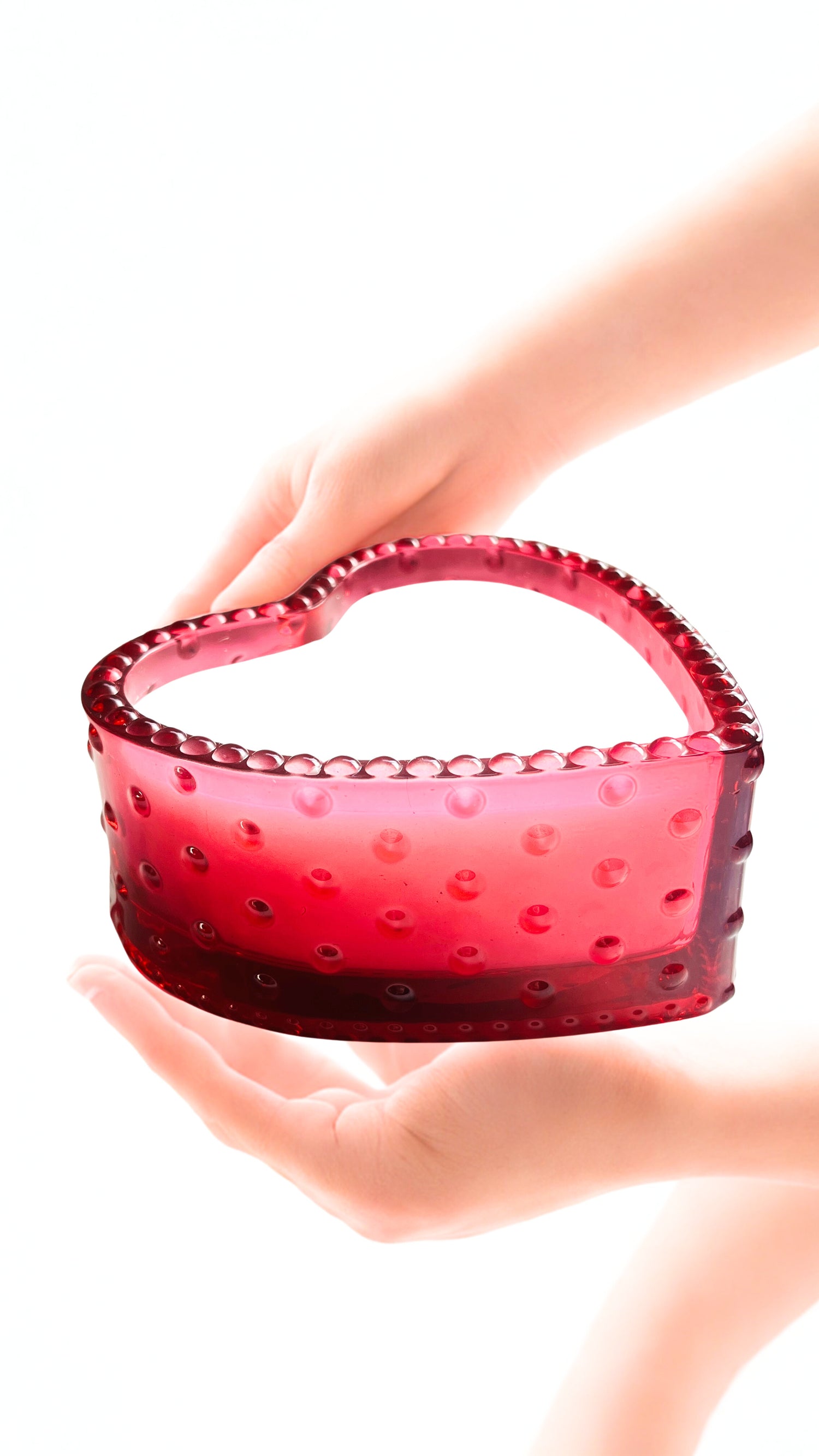 Red glass candle with textured rim held in hands against a white background