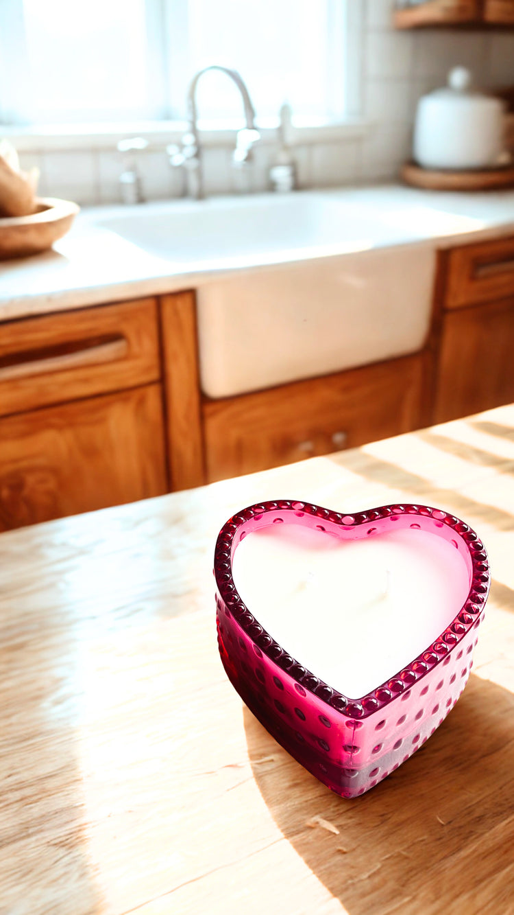 Pink heart-shaped candle on a wooden surface with a kitchen background