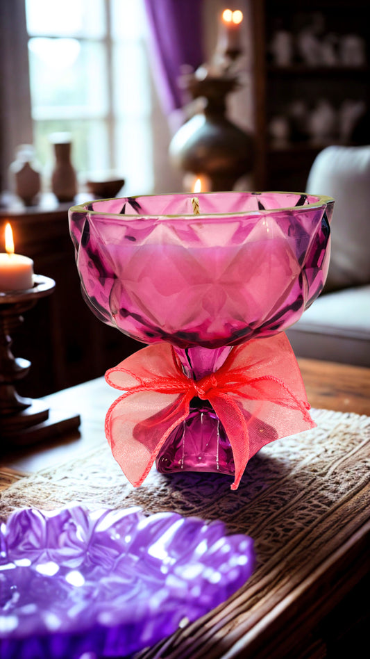 Pink glass goblet candle  with a pink bow on a table in a cozy room.
