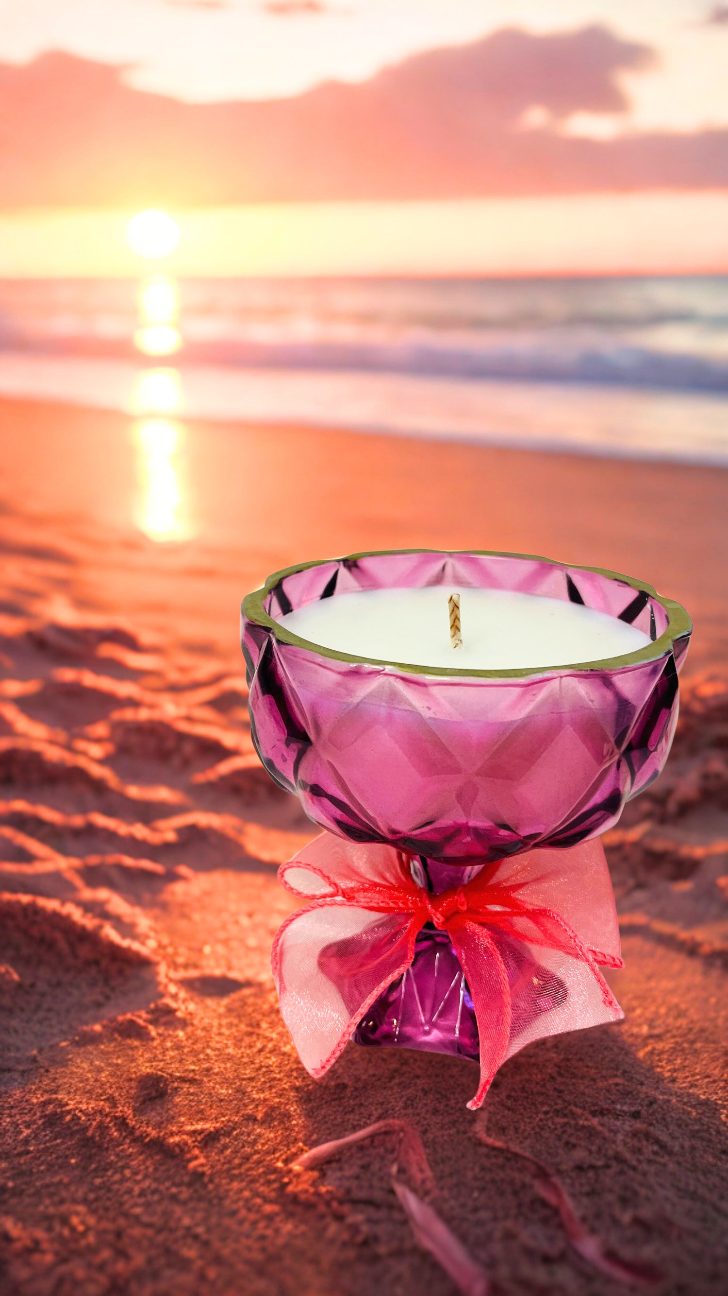 Pink glass candle holder with a pink ribbon on a beach at sunset