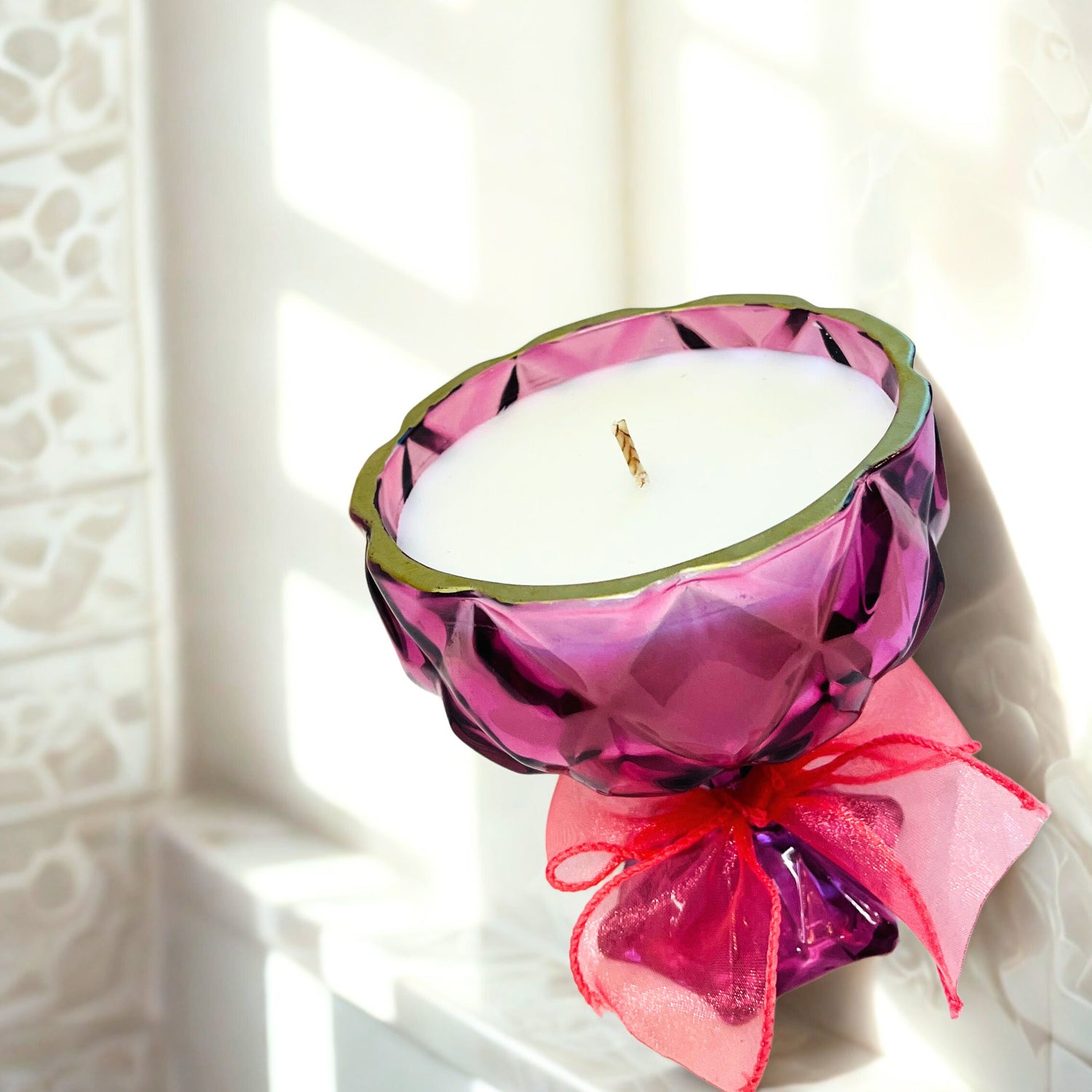 Candle in a decorative pink holder with a bow on a white surface
