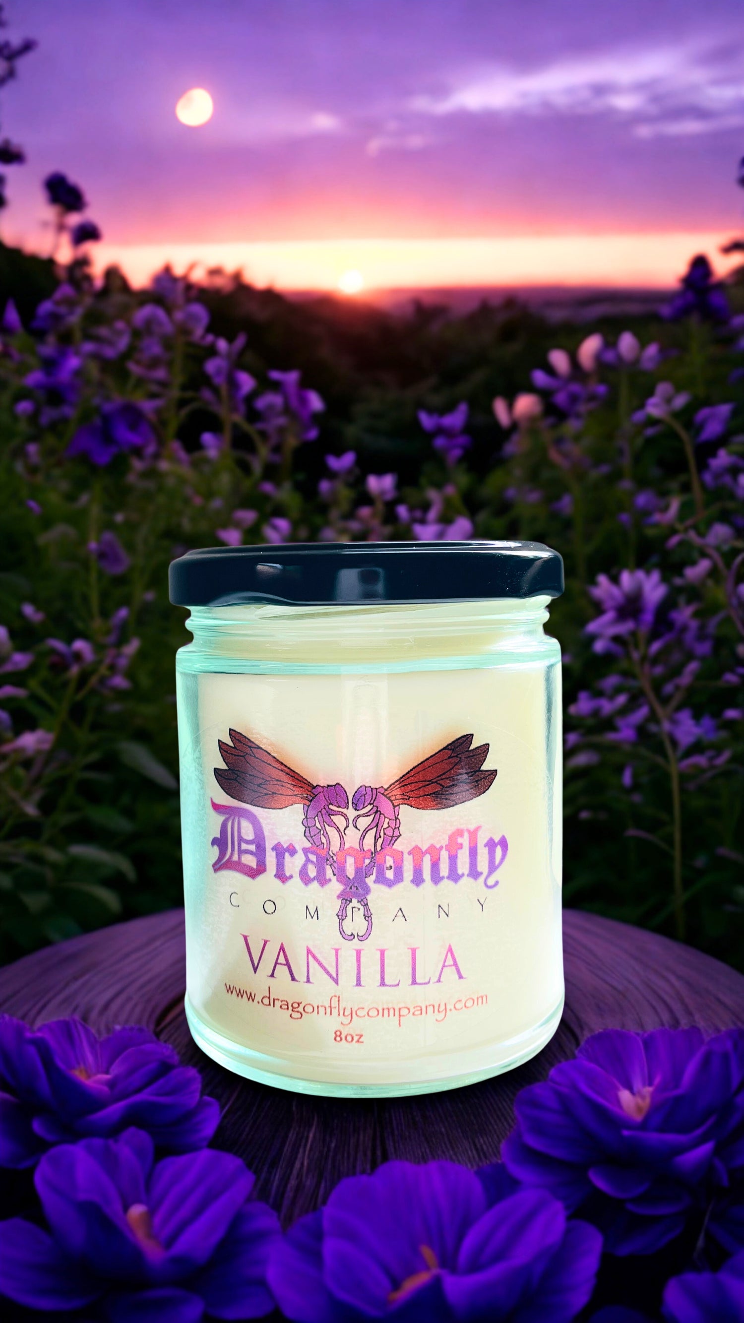 Jar of 'Dragonfly Vanilla' candle with a sunset and purple flowers in the background